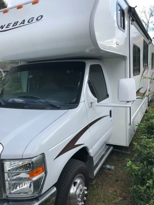 Side view of a white Winnebago RV rental parked, showing its extended mirrors and brown side graphics.. Winnebago Minnie Winnie 2014