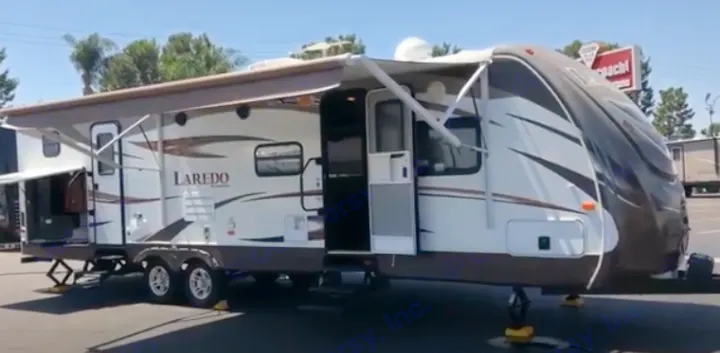 A large white and brown Laredo travel trailer, ideal for RV rental, showcasing its extended awnings and open doors.. Keystone Laredo 2014