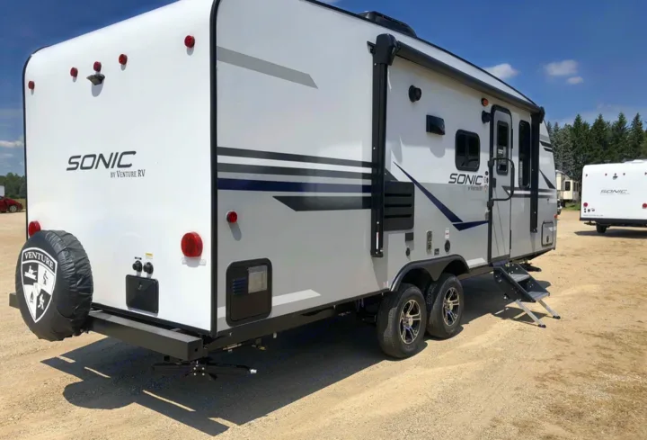 This Sonic by Venture RV travel trailer, ideal for an RV rental, is parked on gravel with extended steps and a spare tire.. Sonic Sonic Trailer 2025