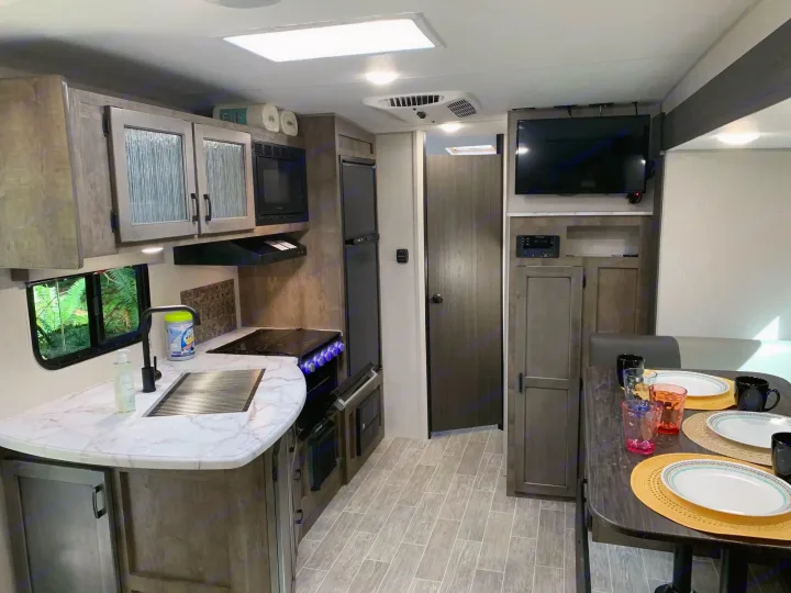Modern RV rental interior: kitchen with stove & sink, dining table set for guests, TV, and warm lighting throughout.. Sonic Sonic Trailer 2025