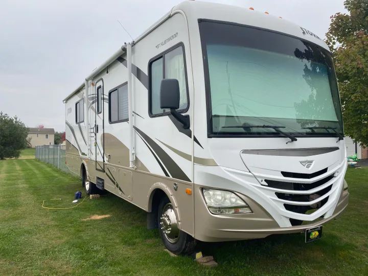 A white & beige Fleetwood Storm RV rental is parked on a grassy lawn, set up with cords and leveling blocks.. Storm Storm Motorhome 2011