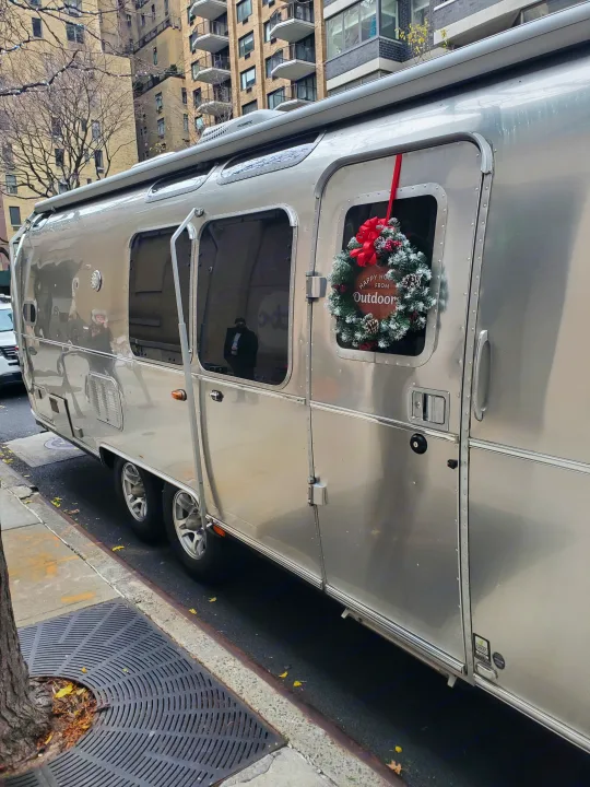 A shiny, silver Airstream rv rental with a festive Christmas wreath is parked on a city street.. Airstream Flying Cloud 2018
