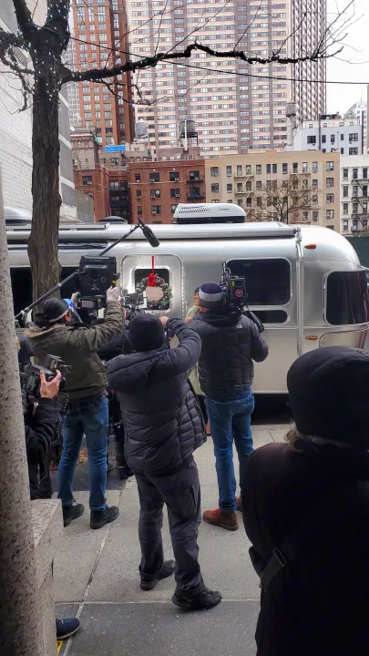 On a city street, a film crew operates cameras and a boom mic, shooting an Airstream RV rental adorned with a holiday wreath.. Airstream Flying Cloud 2018
