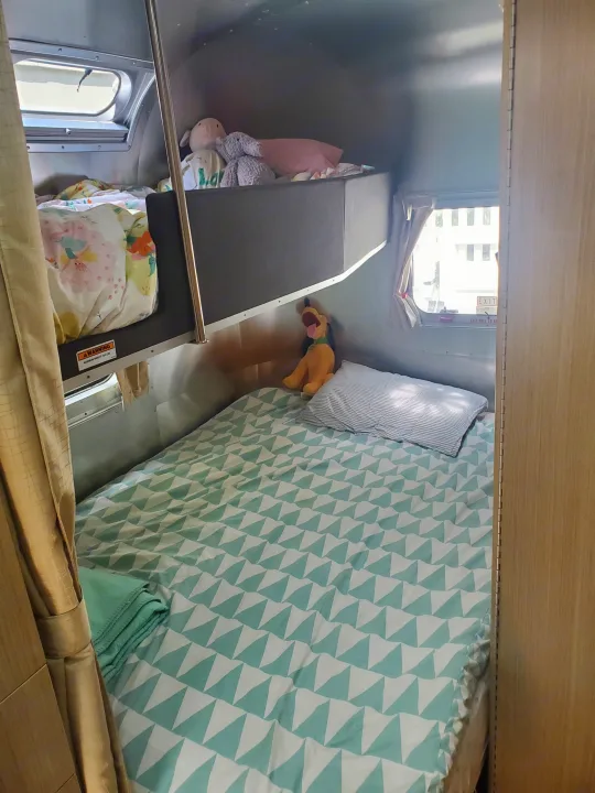 Cozy RV rental interior: a main bed with a teal geometric duvet, a bunk above with floral bedding & plush toys.. Airstream Flying Cloud 2018