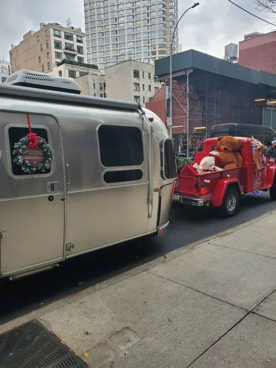Festive Airstream RV rental with holiday wreath, pulled by a red truck carrying stuffed animals on a city street.. Airstream Flying Cloud 2018