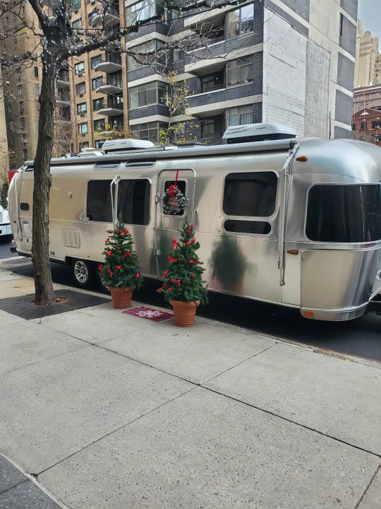 A festive silver Airstream RV rental, decorated with Christmas trees and a wreath, is parked on a city street sidewalk.. Airstream Flying Cloud 2018