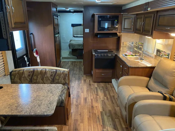 Spacious RV rental interior with a well-equipped kitchen, dining booth, comfy recliners, and bedroom access.. Storm Storm Motorhome 2011