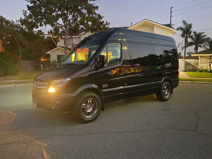 This customized black Mercedes Sprinter van (El Kapitan), ready for rv rental, sits on a quiet street. Headlights gleam.. Mercedes-Benz MB140 2015