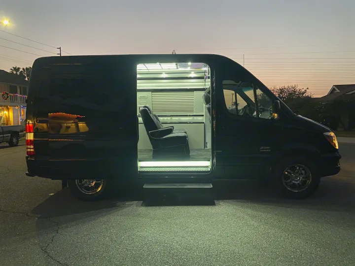 A black luxury Sprinter van RV rental reveals its bright, custom interior through the open side door at dusk.. Mercedes-Benz MB140 2015