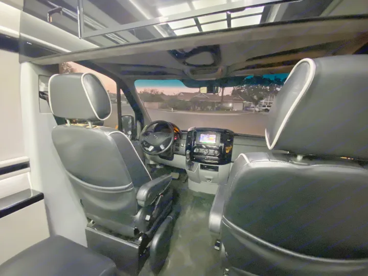 Inside this RV rental: sleek black seats, dashboard, and a clear view of the road at dusk.. Mercedes-Benz MB140 2015