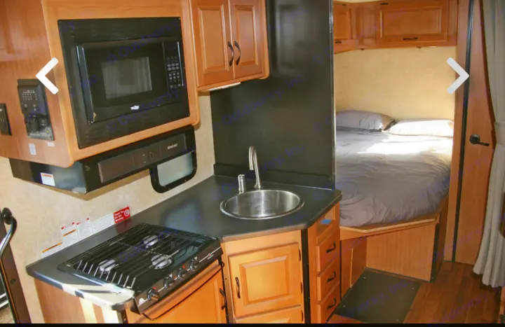 Explore this RV rental's interior! Features a compact kitchen with microwave, sink, stovetop, and a cozy bedroom beyond.. Thor Majestic 2017