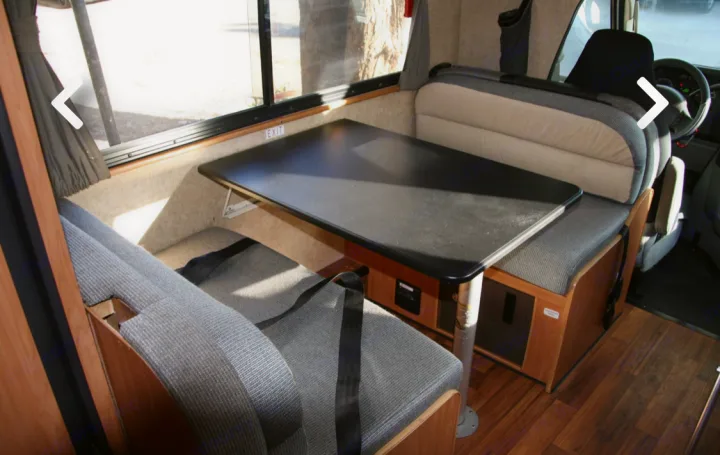 Spacious RV rental interior featuring a dinette with benches and a table, perfect for travel. Large windows and wood floor.. Thor Majestic 2017