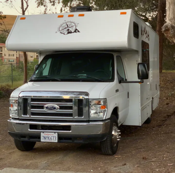 White Ford RV rental parked outdoors, showing the front, side, and California license plate. Compass graphic on cab-over.. Thor Majestic 2017