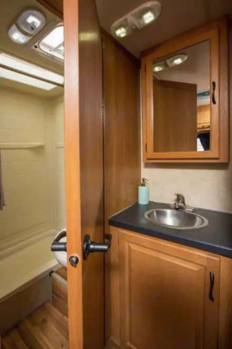 RV rental bathroom with wood vanity, sink, mirror, toilet, and shower. Ideal for your next trip.. Thor Majestic 2017