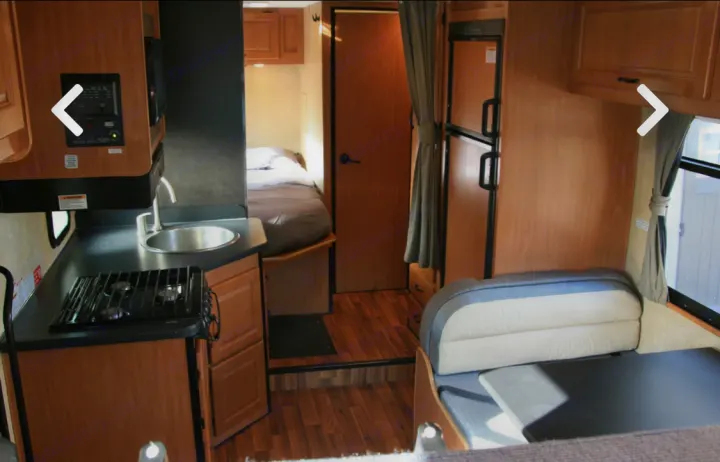 Inside an RV rental: a compact interior featuring a kitchen with sink and stove, a cozy bedroom area, and a dining booth.. Thor Majestic 2017