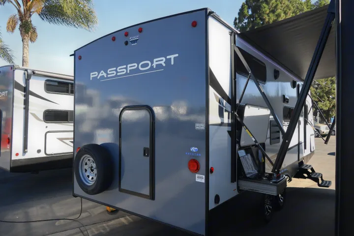 Grey Keyston Passport travel trailer with an extended awning, perfect for an RV rental adventure. Spare tire visible on back.. KeyStone Passport SL 221BH 2022