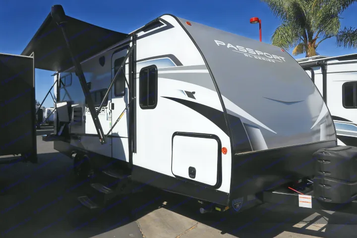 This white and gray Passport SL Series travel trailer with an extended awning is parked outdoors, perfect for your next RV rental.. KeyStone Passport SL 221BH 2022