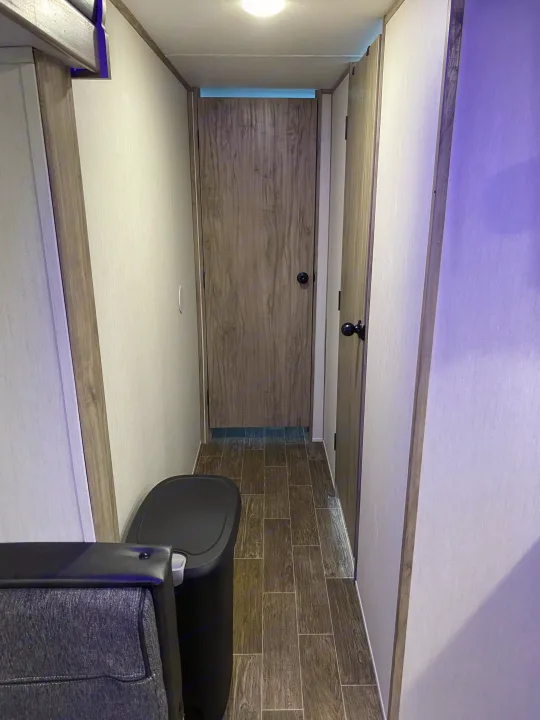 RV rental interior: Narrow hallway with doors, wood-look floor, and a trash can, lit by overhead and accent lights.. Forest River Cherokee Alpha Wolf 2021