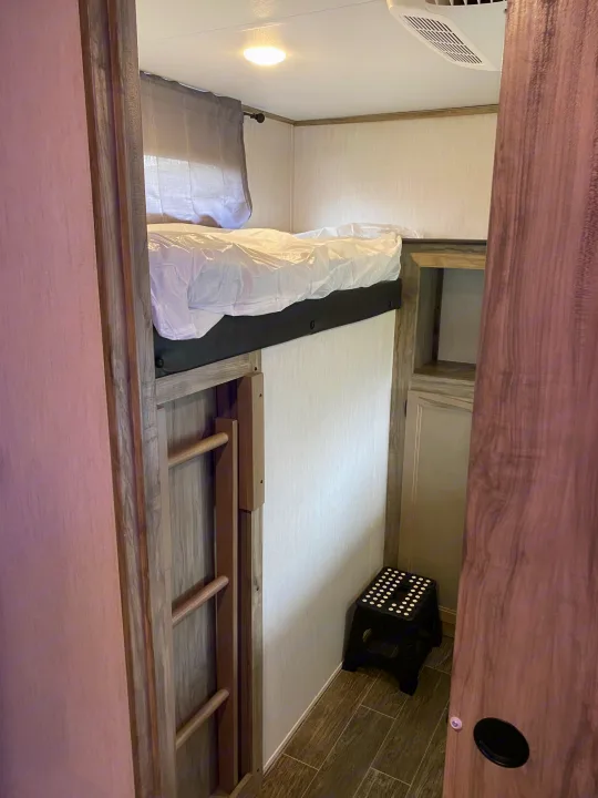 Cozy RV rental bunk bed setup, complete with a ladder and step stool for convenient access.. Forest River Cherokee Alpha Wolf 2021
