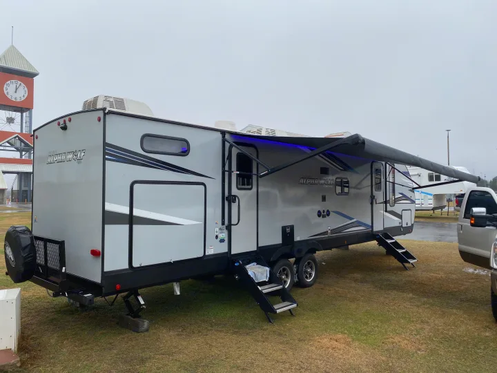 A gray Cherokee Alpha Wolf travel trailer, an ideal RV rental, showcasing its extended awning with blue lights.. Forest River Cherokee Alpha Wolf 2021