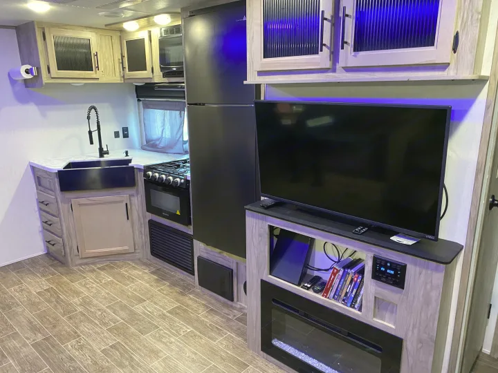 Inside a modern **rv rental**: a well-appointed kitchen with sink & stove, and an entertainment center with TV & fireplace.. Forest River Cherokee Alpha Wolf 2021