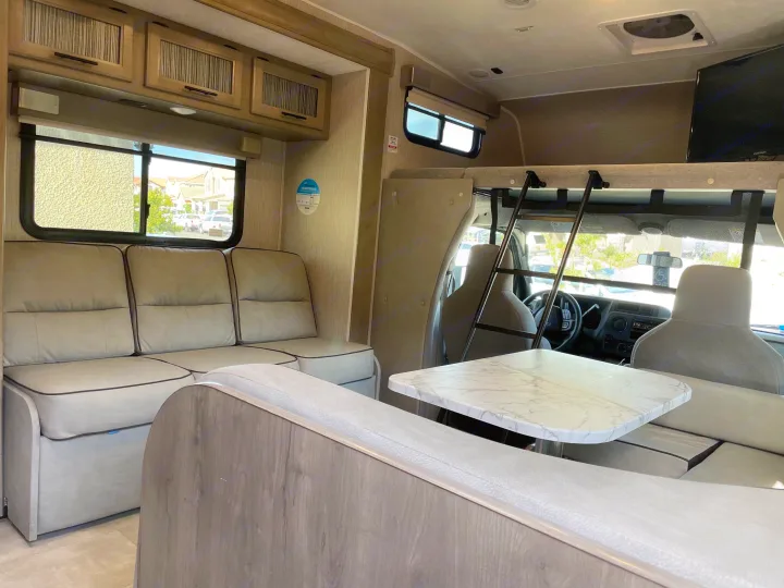 Inside this rv rental: a comfortable living area with a light gray sofa, dinette with marble table, and front bunk bed.. Forest River Coachmen Freelander 2021