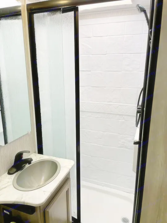 Compact RV rental bathroom: features a frosted glass shower door, textured white walls, and a modern sink vanity with a marble counter.. Forest River Coachmen Freelander 2021