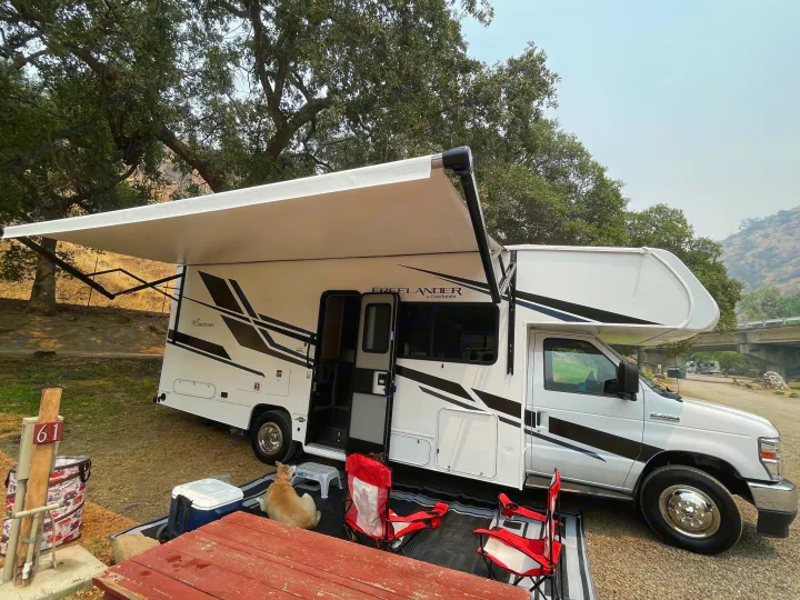White Coachmen Freelander rv rental at campsite 61 with extended awning, picnic setup, and dog. Perfect for camping trips.. Forest River Coachmen Freelander 2021