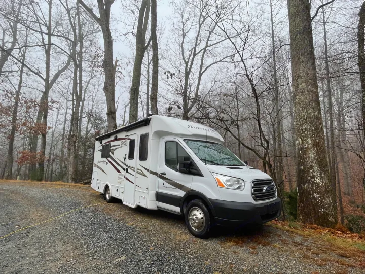 White Sunseeker RV rental parked on a gravel road in a misty forest, surrounded by bare trees.. Forest River Sunseeker 2017