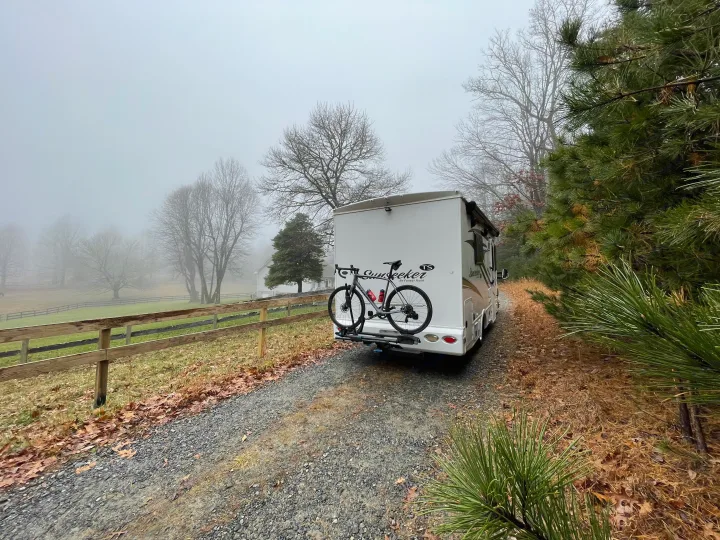 An RV rental with a bike ready for adventure on a foggy day, parked on a gravel path next to a horse fence and misty fields.. Forest River Sunseeker 2017