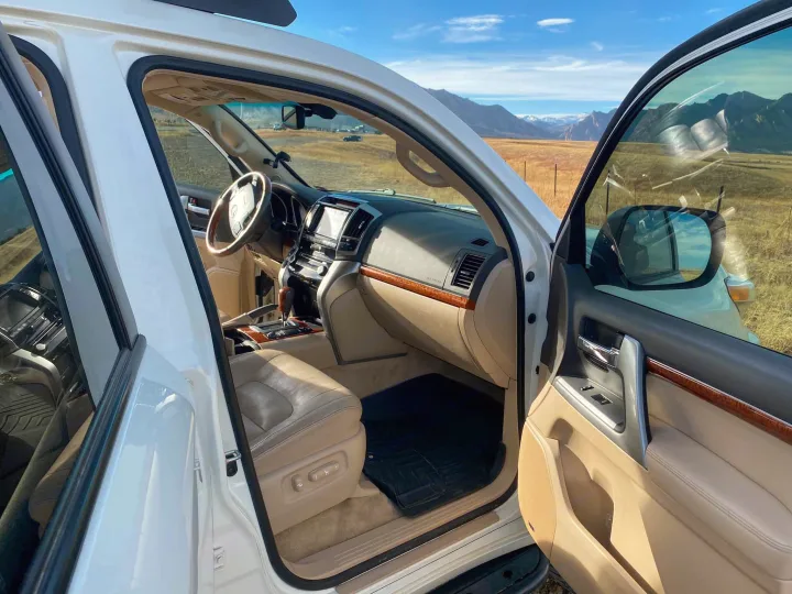 Open white SUV door shows luxury interior and mountain views, perfect for an adventure, often preferred over an RV rental.. Toyota Land Cruiser 2016