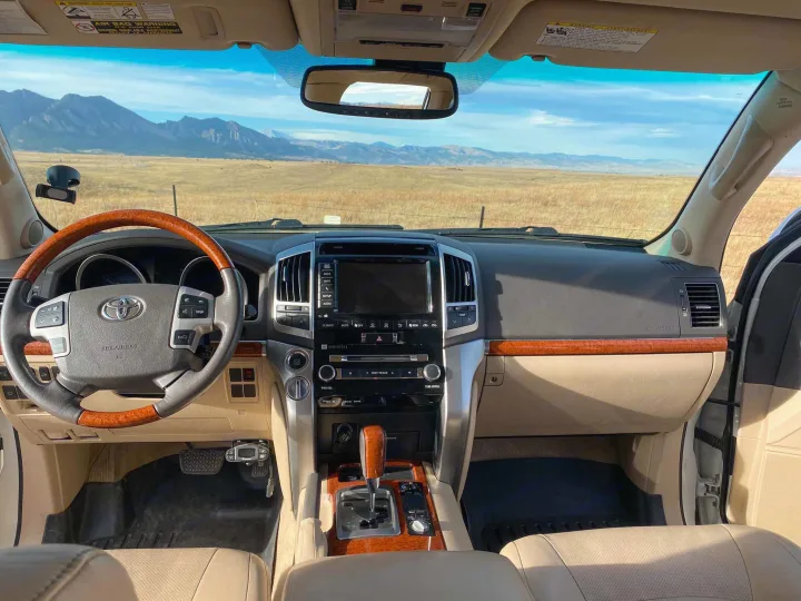 Luxury SUV interior on a road trip, ideal for an RV rental adventure. Stunning mountains & fields ahead.. Toyota Land Cruiser 2016