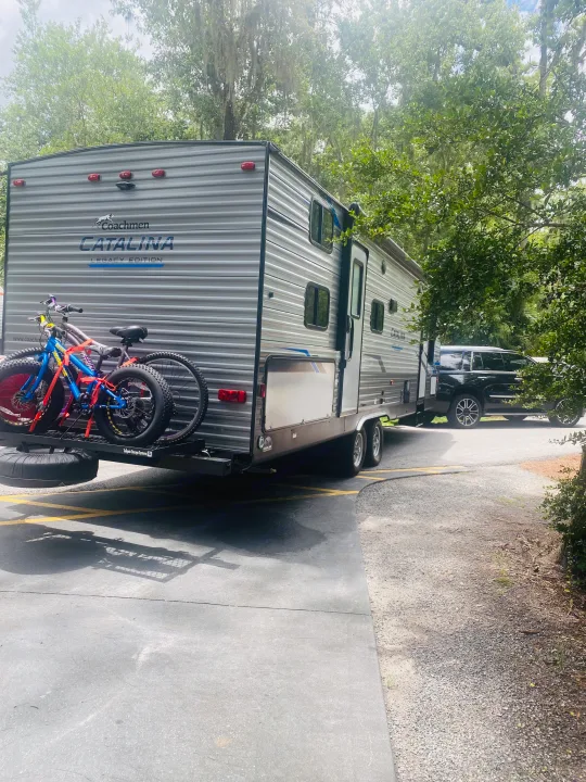 Coachmen Catalina RV rental parked with bikes on the rear, hitched to a black SUV, surrounded by trees.. Forest River Coachmen Catalina Legacy 2021