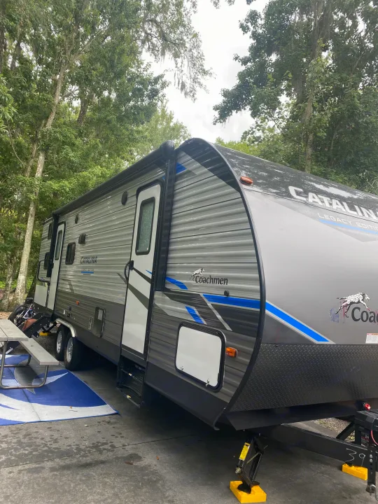 Enjoying an RV rental! A grey Coachmen Catalina travel trailer parked at a shaded campsite, ready for adventure.. Forest River Coachmen Catalina Legacy 2021