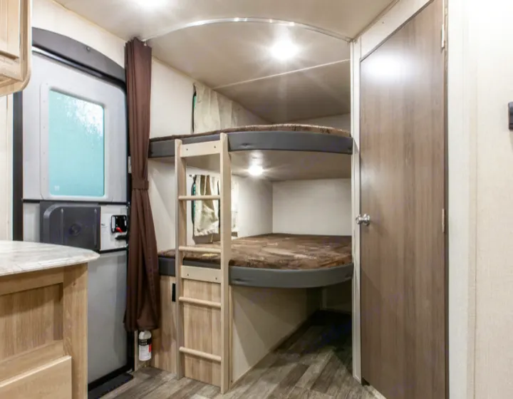 View inside an RV rental showing comfortable bunk beds, an entry door, and a closed interior door to a private room.. Forest River Coachmen Catalina Legacy 2021