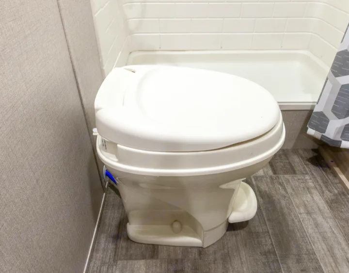 A clean, compact white toilet in an RV rental bathroom, with a shower and tiled walls visible.. Forest River Coachmen Catalina Legacy 2021