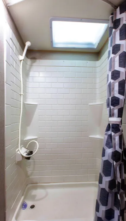 Clean RV rental shower featuring white tile-patterned walls, a handheld sprayer, and a ceiling skylight.. Forest River Coachmen Catalina Legacy 2021