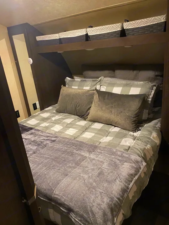 Cozy RV rental bedroom with a grey and white checkered bed, decorative pillows, and overhead storage baskets.. Forest River Salem Cruise Lite 2018