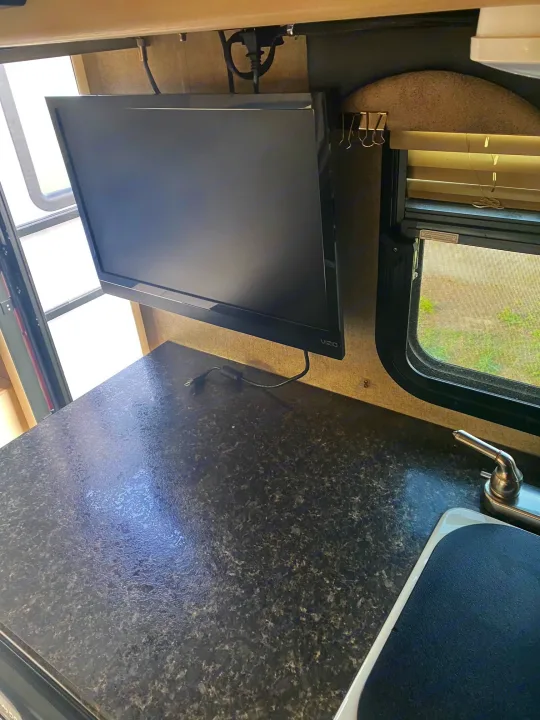 Inside an rv rental: a TV on a shelf, window with blinds, and a dark speckled countertop with a sink.. Winnebago Micro Minnie 2018