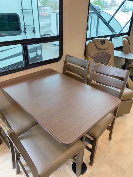 RV rental interior: dining table & chairs, beige captain's chairs, and exterior views of other RVs through large windows.. Grand Design Momentum 2021