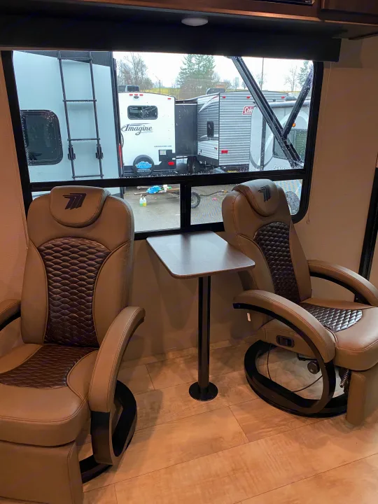 Comfortable RV rental interior: two plush recliners with a table, overlooking other travel trailers.. Grand Design Momentum 2021