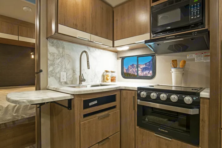 Compact RV rental kitchen with modern appliances: sink, stove, microwave. Features a scenic window view.. Grand Design Imagine 2021
