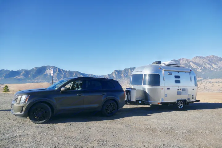 Dark SUV towing a shiny Airstream rv rental on gravel. Mountains and clear blue sky in background, perfect for a travel adventure.. Airstream Caravel 2020
