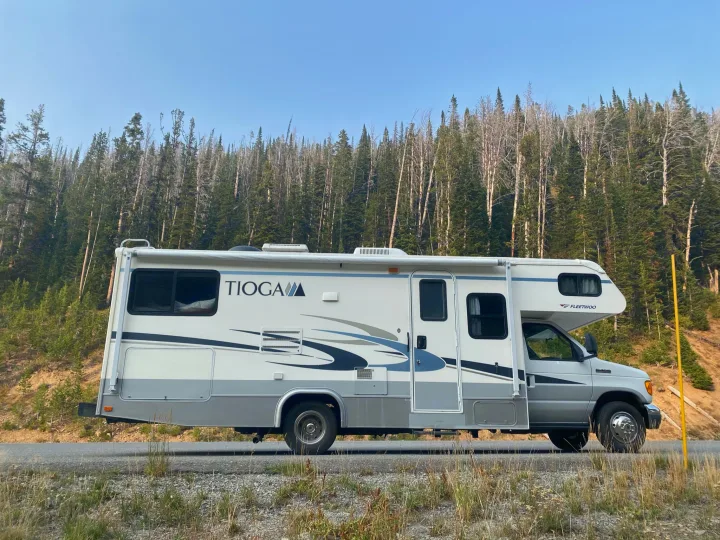A white and grey Tioga Fleetwood RV rental, ideal for a scenic road trip, parked beside a tall forest on a clear day.. Tioga Other 2006