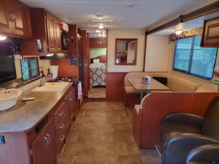 Inside this cozy RV rental: kitchen, dining booth, and peek into the bedroom. A complete home on wheels.. Winnebago Minnie Winnie 2014