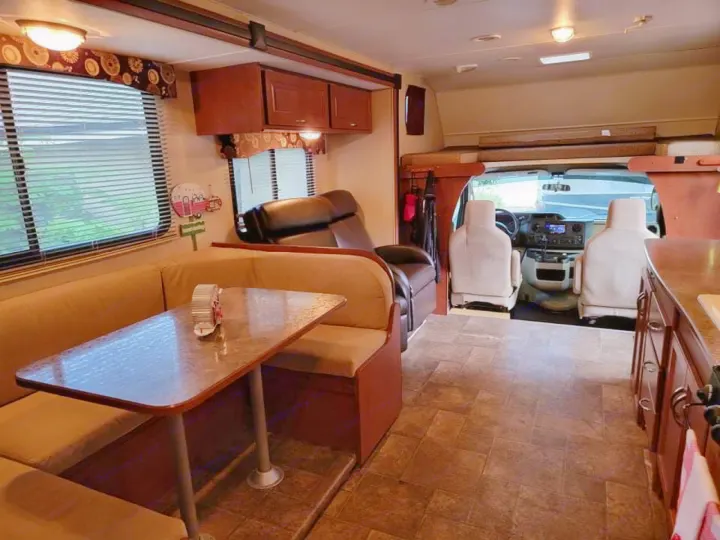 This inviting RV rental interior features a dining booth, full kitchen, comfortable recliner, and front cabin, ideal for travel.. Winnebago Minnie Winnie 2014