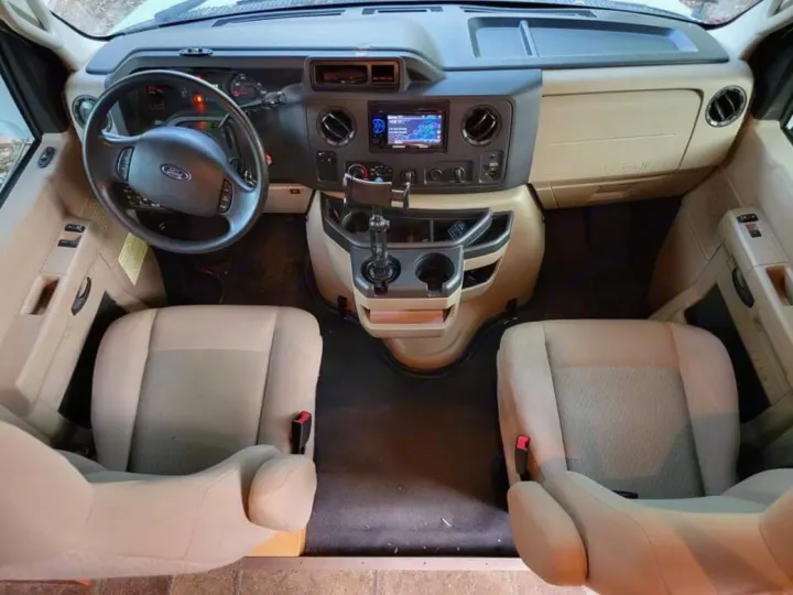 Front cabin of an RV rental, featuring the Ford steering wheel, dashboard with infotainment, and two tan front seats.. Winnebago Minnie Winnie 2014
