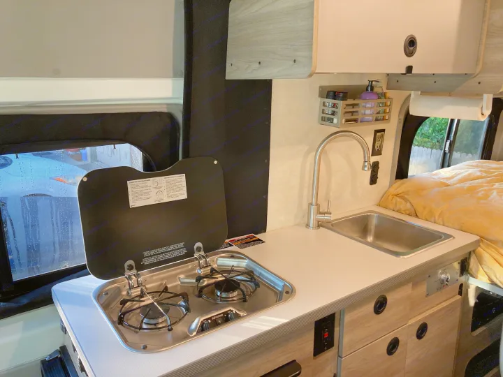 Explore this rv rental's practical interior: a fully-equipped kitchenette with stove, sink, and storage for your adventures.. Winnebago Solis 59PX 2022