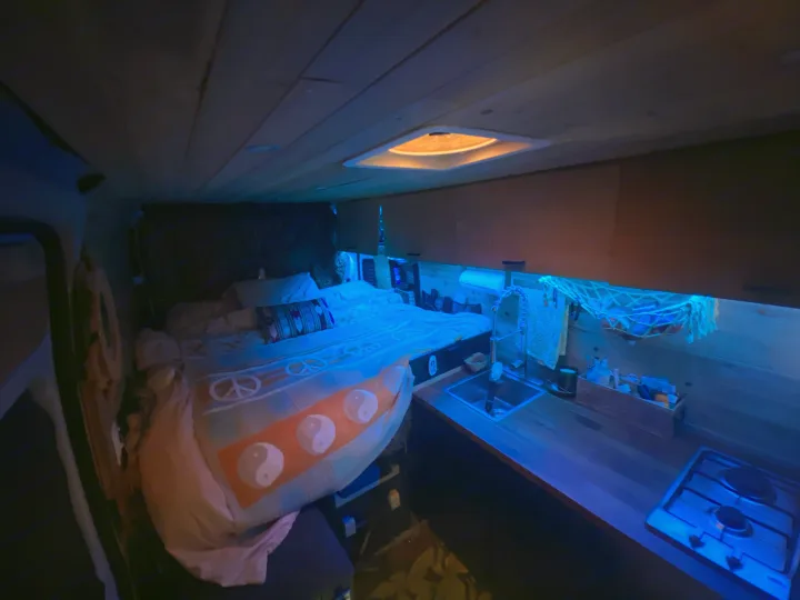 Cozy RV rental interior with bed, sink, and stove, illuminated by blue ambient light. Perfect camper conversion.. Dodge Ram Promaster 2500 2017
