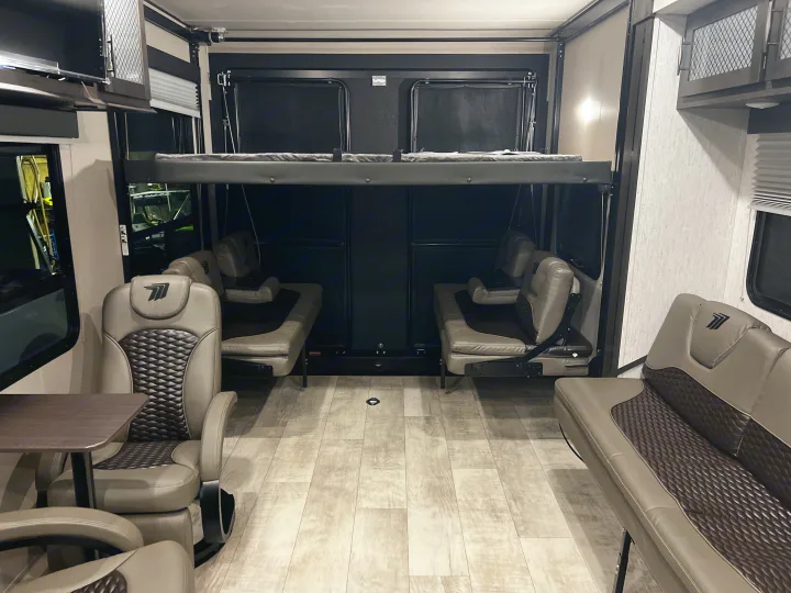 Spacious RV rental interior showing a convertible bunk bed system over adjustable seating, with light wood-look flooring.. Grand Design Momentum 2021